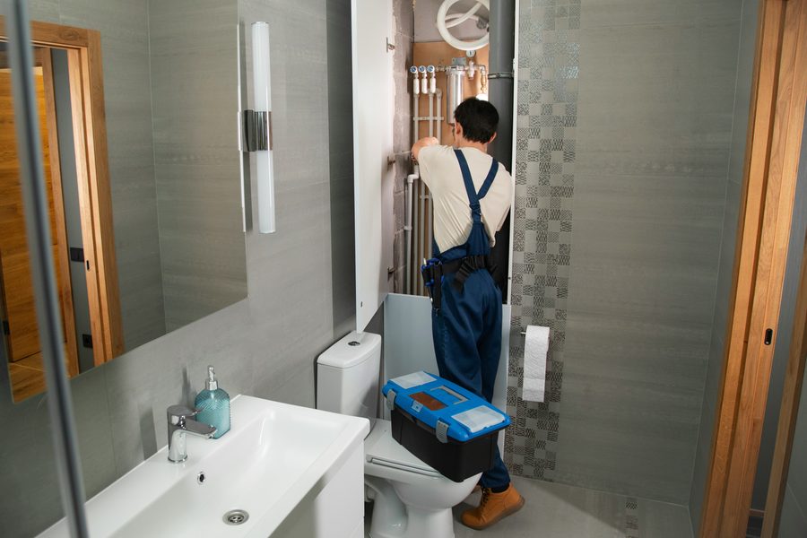 Plumber working on supply piping beside a toilet
